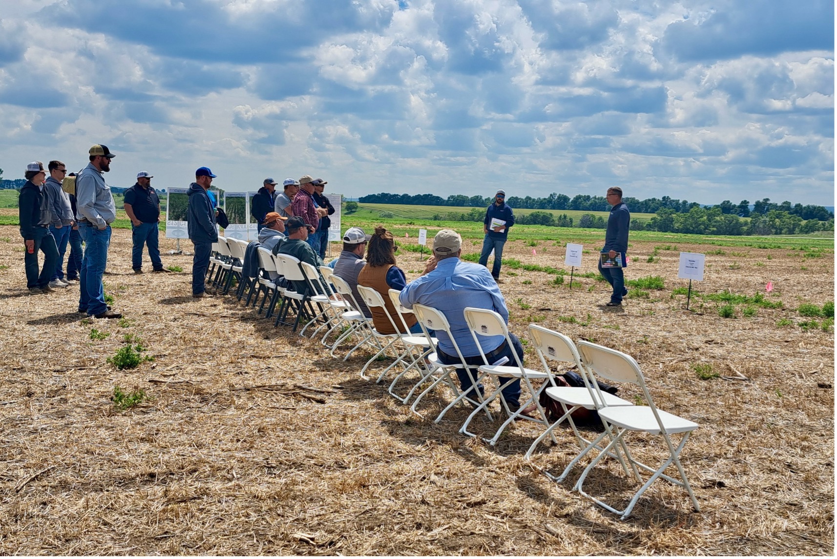 Group of people seated and standing outdoors listening to a presentation at the Answer Plot Innovation Tour